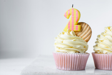 Pink cupcakes with tall american buttercream swirl and a number two candle, cupcakes in pink liners with a tall vanilla buttercream and a candle, birthday cupcakes on a white background