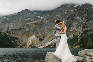 Romantic wedding couple in love standing on the stony shore of the Sea Eye lake in Poland. Scenic...