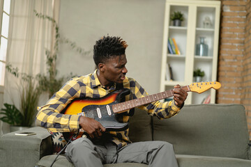 Young joyful african american man playing guitar in living room. Happy man enjoy at home.