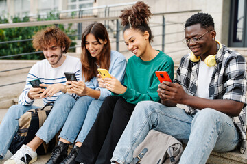 University Students sitting in stairway typing on smartphones - Multicultural group of friends using cellphones 