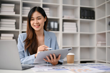 Attractive Asian businesswoman using her tablet and laptop at her desk