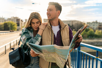 A man is holding a map while a girl is leaning on him, tourists are walking around the city