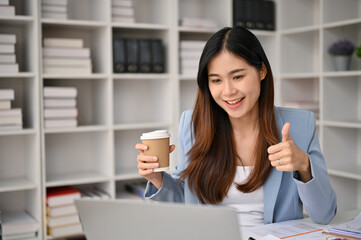 Charming Asian businesswoman giving thumb up to her workers during an online meeting.