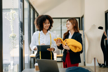 Diverse female fashion designers at work with tailor centimeters on necks and holds tablet and smartphone. independent creative design business. ..