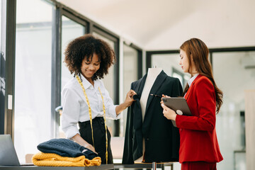 Couple of fashion designers working with fabric and clothing sketches at the studio full of tailoring tools  and holds tablet and laptop. .