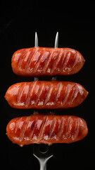 Fried sausages on fork, black background