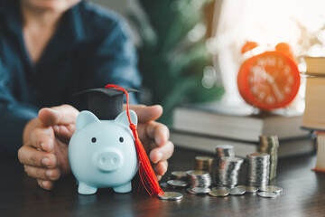 Hands protecting graduation cap on piggy bank with stack coins. Concept of saving money for...