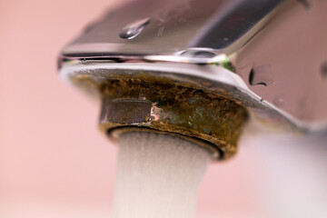 Extremely close up water run and flow from steel faucet. Macro flowing tap water drops and stream on pink background. Water save and water resource problem. Bathroom equipment, plumbing and flooding.