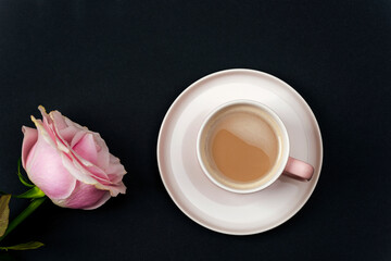 Coffee cup and pink rose on black background. Top view, flat lay
