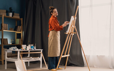 Fototapeta na wymiar Beautiful female painter with easel in art studio. Young talented artist working.