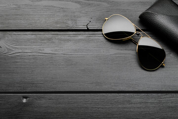 Black plastic classic sunglasses on dark wooden table. Top view, copy space.