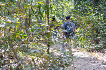 Handsome asian young male traveler with backpack, holding walking stick and hiking stick, standing in the forest with happiness, freedom in summer vacation, travel concept.