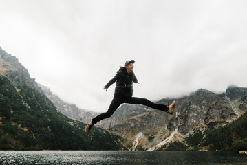 A man jumping on the stony shore of the Sea Eye lake in Poland. Scenic mountain view. Morskie Oko. Tatra mountains.