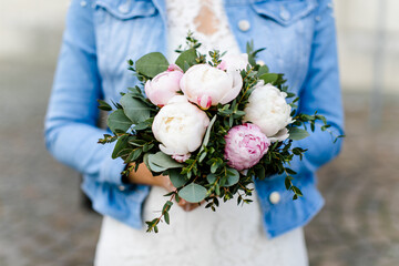 Braut in Jeansjacke hält Brautstrauß mit weiß rosa Pfingstrosen