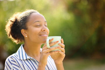Relaxed black woman smelling coffee in a park - obrazy, fototapety, plakaty
