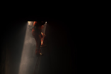 The firefighter carefully descends the ladder one rung at a time into the dark room with soft light.