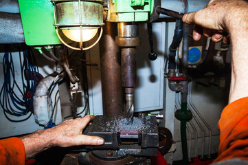 Drilling a steel plate clamped in a vice on a drilling machine.