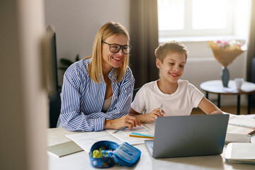 Female babysitter is teaching little boy use laptop application during studying