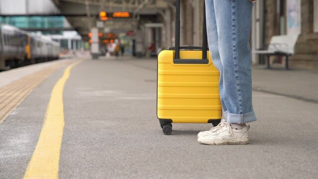 Traveler with a yellow suitcase waiting for a train at the train station on the platform.   Travel concept.