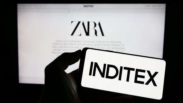 Stuttgart, Germany - 04-16-2023: Person holding mobile phone with logo of Industria de Diseno Textil S.A. (Inditex) on screen in front of web page. Focus on phone display.