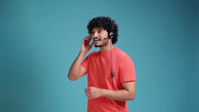 latin spanish male call center operator with head set talking in coral t-shirt on blue studio background