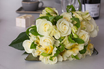 A festive tender bouquet with light roses on the table on a bottle of wine and a gift box