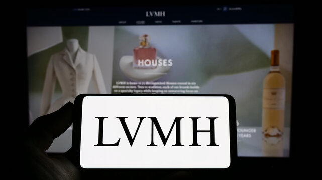 Stuttgart, Germany - 04-16-2023: Person holding smartphone with logo of  company LVMH Moet Hennessy Louis Vuitton SE on screen in front of website.  Focus on phone display. Stock Photo
