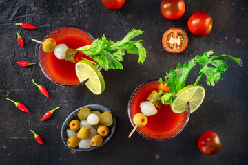 Bloody Mary cocktail with garnish on a black background, overhead flat lay shot. Spicy tomato juice with alcohol, lime, pickles, celery, and peppers