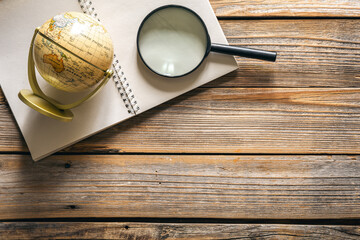 Earth globe, magnifier and notepad on wooden background, top view.
