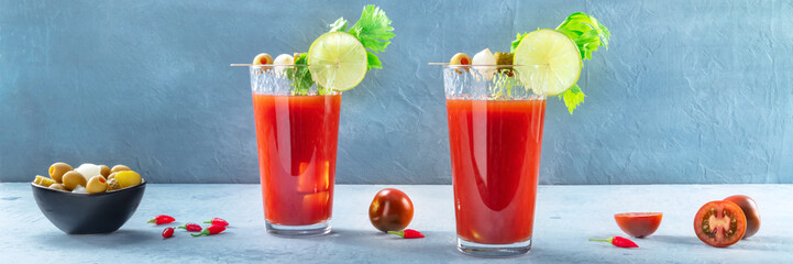 Bloody Mary cocktail with garnish panorama on a blue background. Spicy tomato juice with alcohol, lime, pickles, celery, and peppers