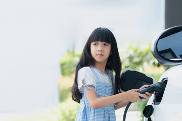 A playful girl holding an EV plug, a home charging station providing a sustainable power source for...