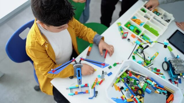 Robotics programming class. Children construct and code Robot. STEM education using constructor blocks and laptop tablet, remote control joystick. Technology educational development for children