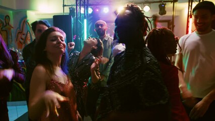 POV of cheerful persons enjoying dance party at nightclub, having fun together on funky music. Young people jumping and partying on dance floor, dancing under spotlights. Handheld shot.