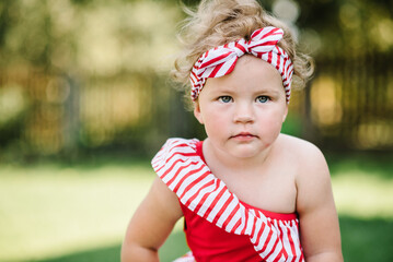 A lovely girl in a red and white bathing suit stands in a field. Child in the summer garden. Kid in the backyard, outdoor lifestyle. Close up.