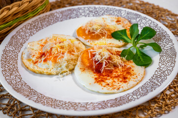 fried egg sprinkled with grated horseradish and red pepper, leaf on white plate.