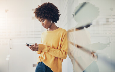 Young businesswoman leaning against a glass wall and texting on her mobile
