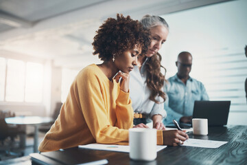 Diverse businesswomen reading through paperwork together at an office table