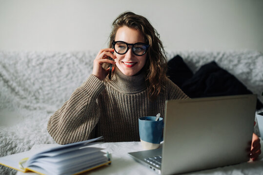 Young Accountant Manager Working At Home At The Kitchen Table, Talking On The Phone In Front Of The Laptop, Smiling, Cute Talking To CEO Or Bank Support Team About Corporate Account