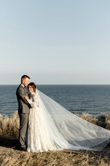 the groom with a beard hugs the happy bride under the veil. meeting of the bride and groom in nature overlooking the sea. wedding walk.