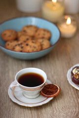 Books, reading glasses, e-reader, plate of chocolate pralines, bowl of cookies, cups of tea and lit candles on the table. Selective focus.