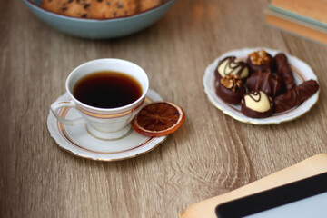 Books, reading glasses, e-reader, plate of chocolate pralines, bowl of cookies, cups of tea and lit candles on the table. Selective focus.