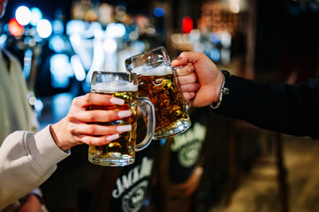 man and woman hands clinking with glasses of light beer at the pub or bar