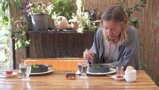 A hippie woman eats breakfast in the summer on the veranda with a friend
