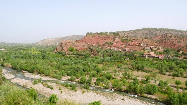 Rural village in valley with lush vegetation and river in Morocco, high angle