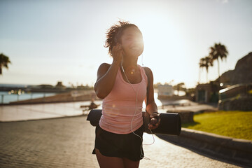 Smiling woman walking with a yoga mat listening to music