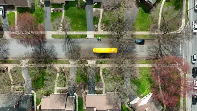 Aerial top down tracking of school bus driving through American suburb. Residential homes and houses in community with students.
