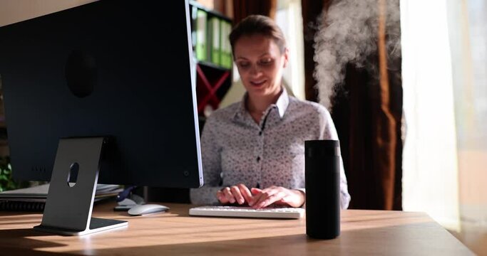 Modern air humidifier device during sedentary workplace. Woman freelancer using computer work on internet enjoying aromatherapy steam from essential oil diffuser in home office room