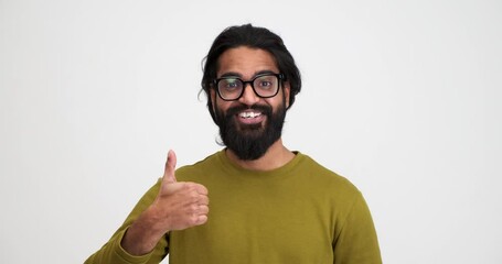 Slow motion shot of bearded cheerful young man shaking head and showing thumbs up sign while standing over white background