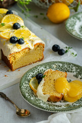 Slice of homemade lemon pound cake decorated with cream cheese frosting, fresh lemon slices and blueberries with lemon curd on green vintage plate on linen tablecloth.