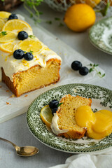 Slice of homemade lemon pound cake decorated with cream cheese frosting, fresh lemon slices and blueberries with lemon curd on green vintage plate on linen tablecloth.